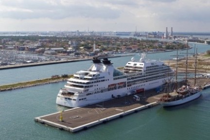 Two cruise ships docked at a pier in a harbor with a city in the background.