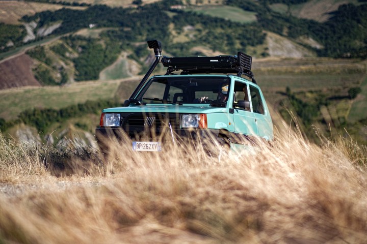 Light blue vintage car parked in a grassy field with hills in the background.