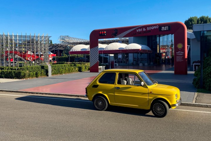 Yellow vintage car parked in front of a building with a red arch and glass entrance.