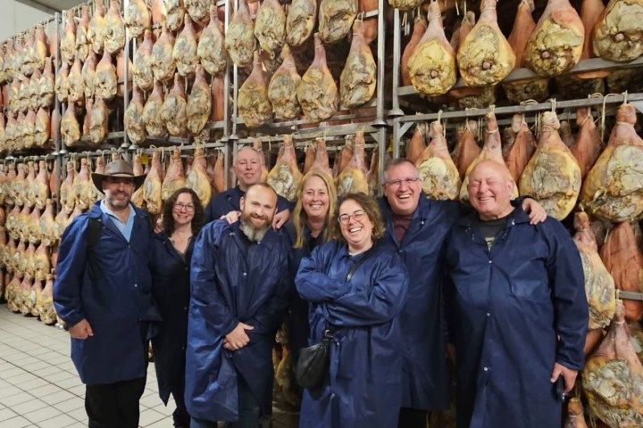 Group of people in blue coats posing in front of hanging cured meats.
