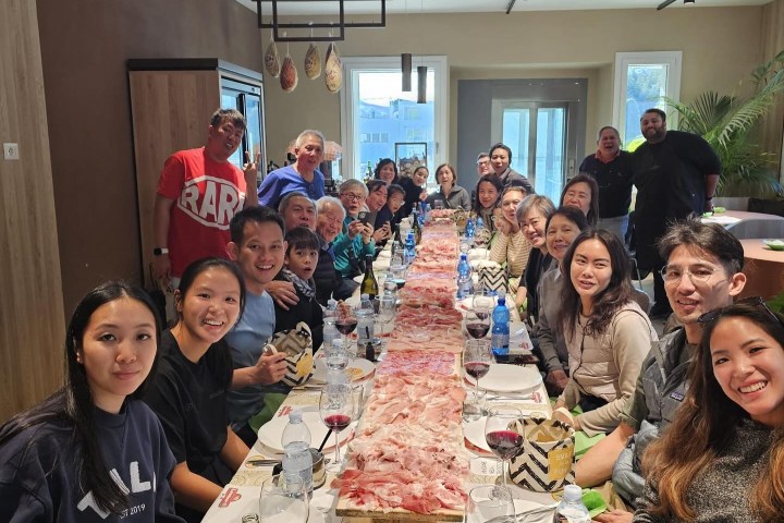 Large group of people sitting at a long table with plates and drinks, smiling at the camera.