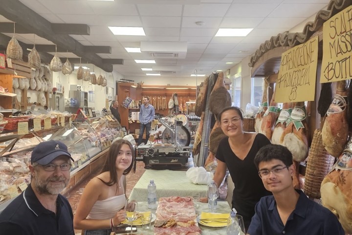 Four people at a deli table with sliced meats and bottles of water.