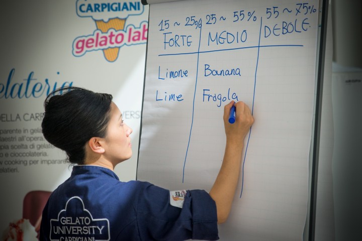 Person writing gelato flavors on a flipchart at a gelato workshop.