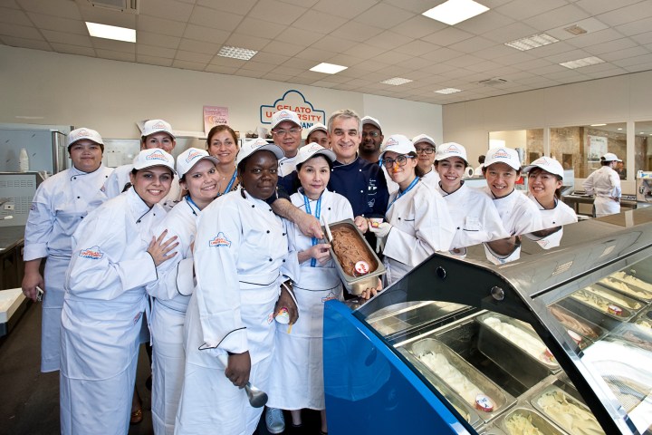Group of chefs in white uniforms posing with gelato in a kitchen setting.