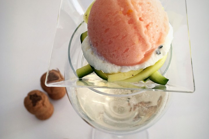 Peach sorbet with cream and zucchini garnish in a glass, surrounded by brown cookies.